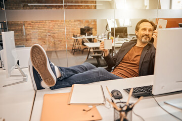 Smiling adult office worker with beard using smartphone in loft office