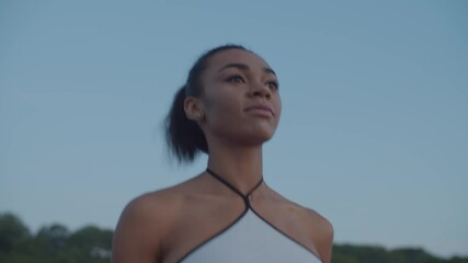 Portrait of attractive confident black female athlete in sports clothes running outdoors in early morning over blue sky in background. Sporty fit attractive african woman jogging outside at sunrise.