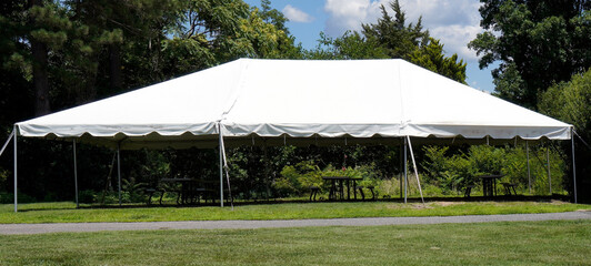 Empty event tent with trees and blue sky in the background and a grassy foreground.