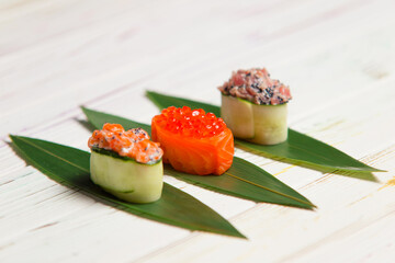 Set of Japanese Gunkan Maki Sushi Rolls: Sake with salmon caviar, tuna Maguro and salmon in cucumber served on bamboo leaves. Pan Asian dishes. Expensive seafood restaurant meal side view

