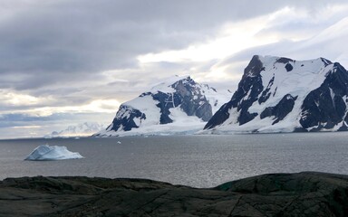 Iceberg in bay with mountains and clouds in antarctic sea, Antarctica