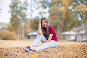 Beautiful Asian women in red dresses and blue jeans sitting in the garden. Portrait of asian woman is smiling on the green grass.