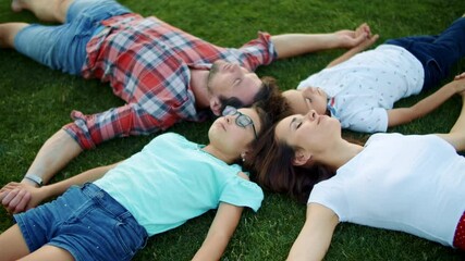 Family lying on green grass in circle. Cute kids and parents relaxing in field - Powered by Adobe