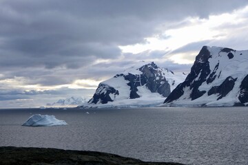 Fototapeta na wymiar Iceberg in bay with mountains and clouds in antarctic sea, Antarctica