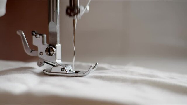 slow mo needle sewing machine sewing white cotton fabric with a needle. The needle of the sewing machine sewing white fabric.
