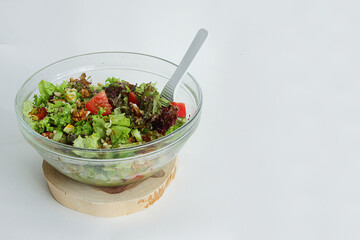 fresh vegetable salad tomatoes, cucumbers, lettuce leaves, pine nuts, walnuts in a glass plate with a white spoon on a wooden stand on a white background and there is a place for the inscription 