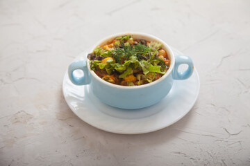 Bean soup with vegetables and cheese in a blue porcelain cup on a light concrete background. Vegetarian cuisine.