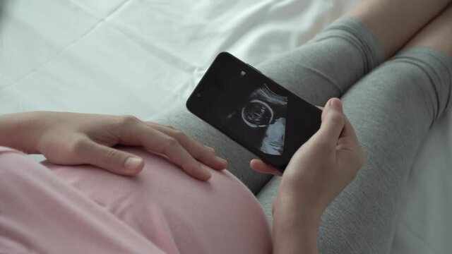 Happy Pregnant woman looking ultrasound image via smartphone