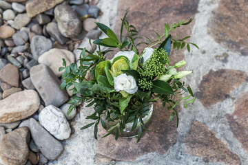 
Bridal bouquet of white eustomas and greenery in a glass vase on sea stones from a high angle.