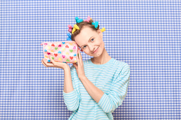 Happy girl with colorful hair curlers on head is holding cosmetic bag