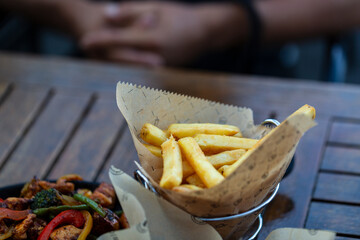 Fried chicken with  french fries in a paper wrapper on wooden background with copy space for your text, shallow focus