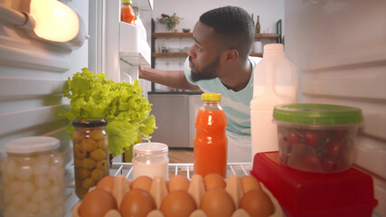 African young guy looking for meal to eat in fridge