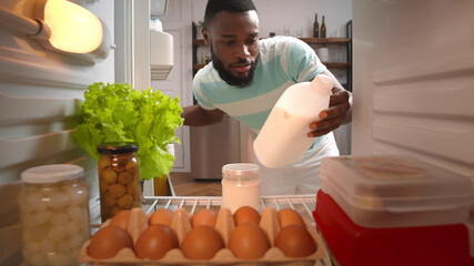 African male taking bottle of milk from full fridge