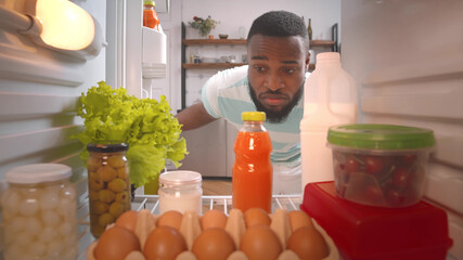African guy in earphones opening fridge to take drink