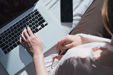 Woman with wounded arm sits in bed next to a computer and phone. Concept of remote work, not being able to be productive, staying on a sick leave