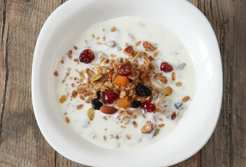 Granola (muesli) for breakfast with oatmeal, various seeds and dried fruits in a white plate with milk. Healthy and delicious diet breakfast.