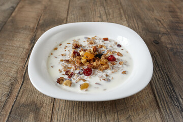 Granola (muesli) for breakfast with oatmeal, various seeds and dried fruits in a white plate with milk. Healthy and delicious diet breakfast.