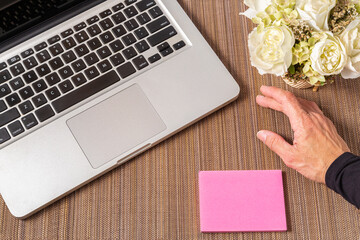 mesa de trabalho com mão feminina, um laptop, bloco de anotações em branco e um vaso de flores 