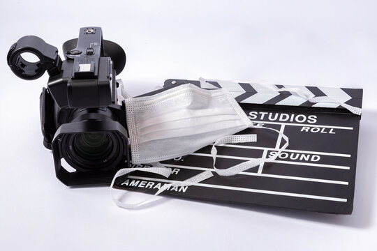 Uma câmera de filmagem, uma máscara e uma claquete  no fundo branco é o novo normal das produções audiovisuais 