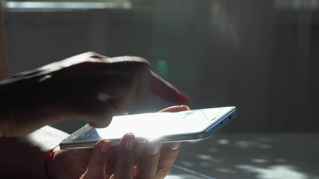 close up woman hand holding wite telephone smart phone screen golden sun light sunshine background sunny day internet searching application store notification weblink online video call