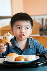 Little boy eating fried chicken drumstick in a cafe.