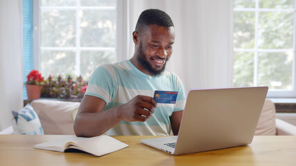 African young man using laptop and credit card paying bills online
