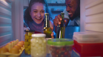 Obraz na płótnie Canvas Happy couple taking beer bottles from refrigerator