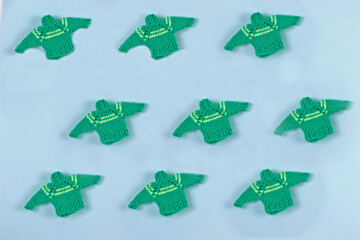 Many small green knitted sweaters background.Christmas pattern made of wooly jerseys on blue table. Holiday xmas backdrop.Winter concept. Flat lay.