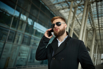 Urban business man in sunglasses talking smart phone traveling walking outside airport. Casual young businessman wearing suit jacket. Handsome male model in 20s, Manager, City Hall, cell.