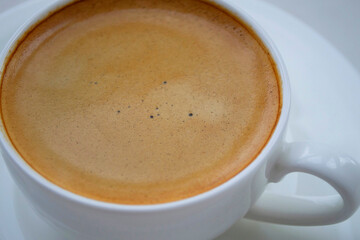 Coffee in a white cup close-up. Against a light background, in natural daylight. Focus is specially set on the bubbles of a coffee drink in the center