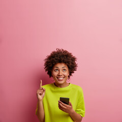 Amused cheerful African American woman holds modern mobile phone, connected to free internet,...