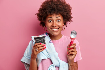 Beautiful cheerful African American woman eats tasty ice cream during summer time, holds spoon and...