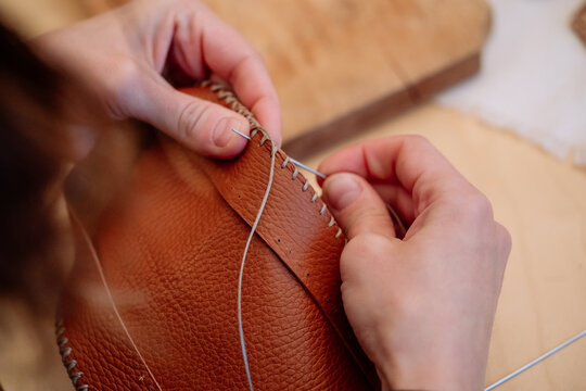 Detail shot of woman's hands sewing a brown piece of leather with a needle