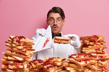 Restaurant worker in elegant white clothes, holds tasty sandwich made of bread and jam, dirty...