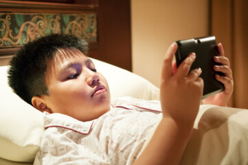 Young boy lying in bed with tablet in hands