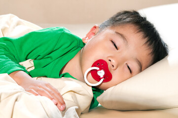 Young boy asleep with pacifier in bed.