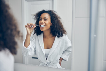 Pleased curly-headed pretty lady brushing her teeth - Powered by Adobe