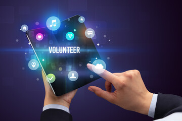 Fototapeta premium Businessman holding a foldable smartphone with VOLUNTEER inscription, social media concept