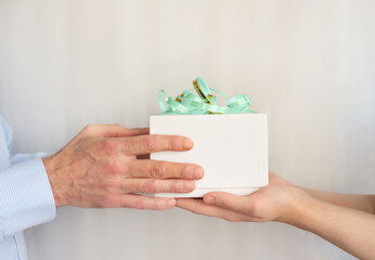 Son gives dad a gift for father's Day. Close-up of a man's hand with a white box, with a bow, on a light background. Selective focus, space for copying. Concept February 23, Christmas