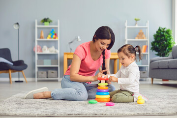 Hispanic mother and daughter play with toys while sitting on the floor in the room.