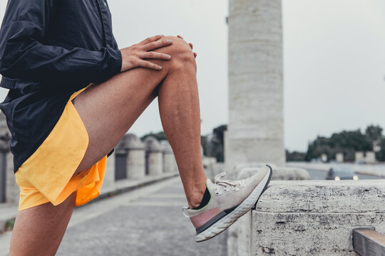 Dettaglio di atleta che pratica piegamento della gamba poggiato al bordo di una strada urbana deserta