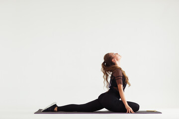 Beautiful sporty yogi girl practices yoga asana, stretching exercises on grey background, low key...