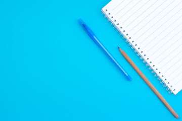 Back to school. The view from the top: a notebook on a spring, pen and pencil on a blue background. Horizontal position, space for text, flat lay
