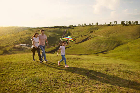 Adorable Little Girl Flying Kite While Her Parents Walking Behind Her In Mountains During Camping Trip. Family Vacation