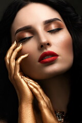 Close-up portrait of beautiful young woman with bright red lipstick and golden hands