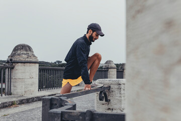 Giovane uomo atletico e sportivo pratica esercizi di stretching in solitudine in una strada deserta di città