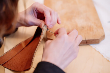 Detail shot of woman's hands sewing a brown piece of leather with a needle