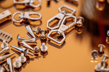 Obraz na płótnie Canvas Silver handbag accessories, rivets, screws, carabiners placed on a gold reflective plate