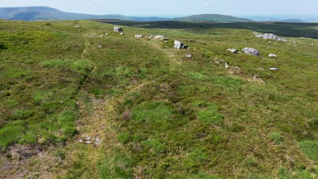 Low aerial view of remote moorland revealing the entrance to an isolated underground cave system. (Chartist Cave, South Wales, UK)