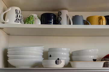 Opened kitchen cabinet with storage plates inside, mugs, bowls and cups